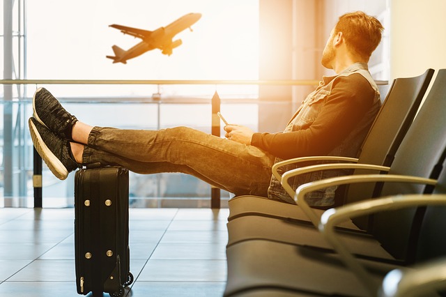 Muž sediaci v letiskovej hale sledujúci odlietajúce lietadlo