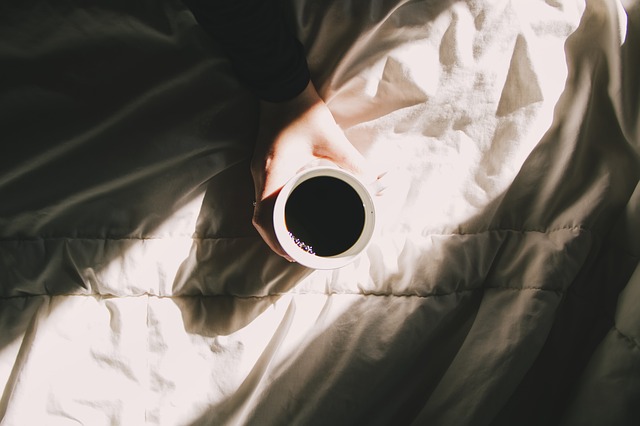 Človek drží hrnček s kávou položený na posteli.jpg